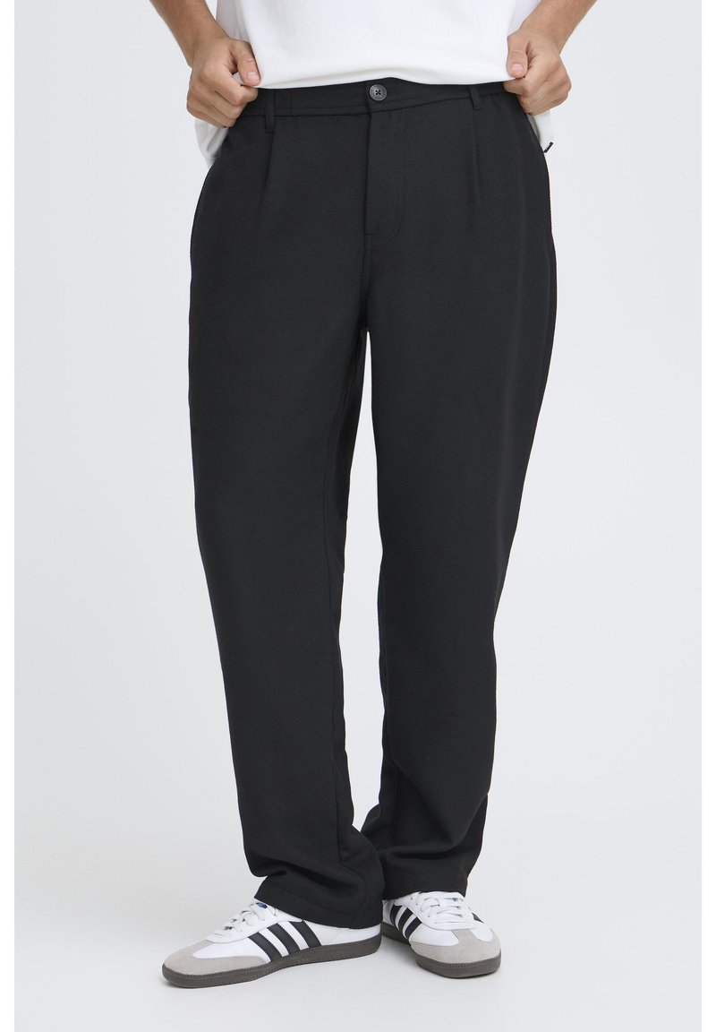 Pantaloni negri plisați cu închidere cu nasturi, prevăzuți cu talie și buzunare laterale; realizați dintr-un material moale, cu croială lejeră.