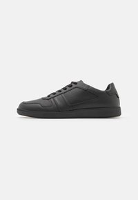 Sneaker sportive nere realizzate in materiale sintetico liscio con accenti perforati, lacci piatti e suola in gomma.