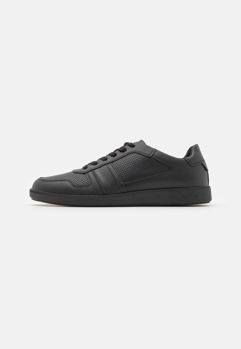 Sneaker sportive nere realizzate in materiale sintetico liscio con accenti perforati, lacci piatti e suola in gomma.