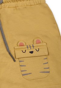 Pantalones cortos de algodón amarillos con una textura suave. Presenta un diseño de bolsillo que asemeja la cara de un oso con detalles bordados. Incluye cintura elástica.