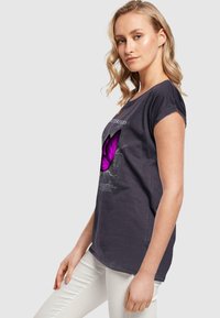 Dark gray t-shirt with short sleeves, featuring a large pink butterfly graphic in the center, and text detailing above the design.