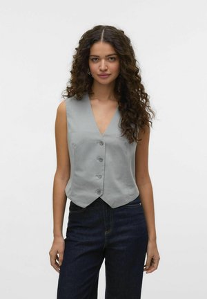 Gilet sans manches gris avec un col en V, cinq boutons et un design ajusté à la taille, associé à un jean bleu marine. Texture de tissu lisse.