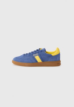 Baskets en suède bleu avec des accents jaunes, dotées d'une semelle en gomme, d'un design à lacets et d'un logo sur le côté. Style sportif classique.