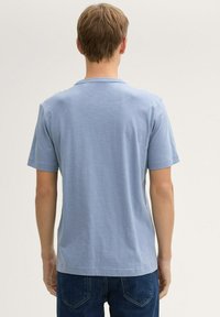 Tricou cu mânecă scurtă, de culoare albastru deschis, dintr-un material moale și ușor. Prezentând un guler rotund și o croială relaxată, cu detalii minime ale cusăturii la spate.