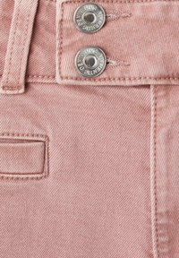 Tejido de mezclilla rosa con un primer plano de dos botones metálicos plateados, un pequeño bolsillo y detalles de costura visibles.