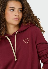 Bordeaux hætte sweatshirt med snøre, der har en lille gylden hjertebrodering på brystet. Fremstillet af blødt bomuldsblandingsstof.