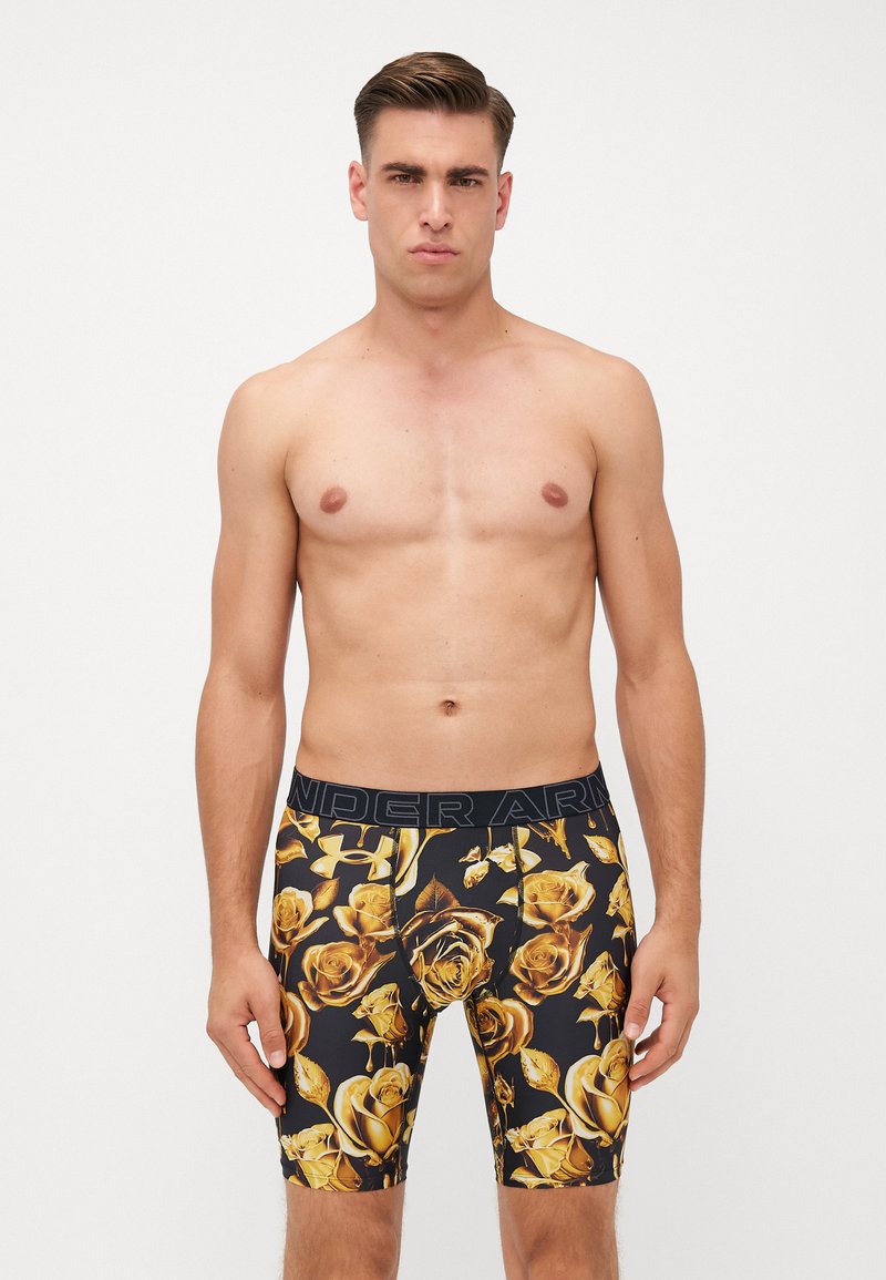 Black boxer shorts with gold rose pattern, made from stretchy fabric. Features comfortable waistband with “Under Armour” logo at the top.