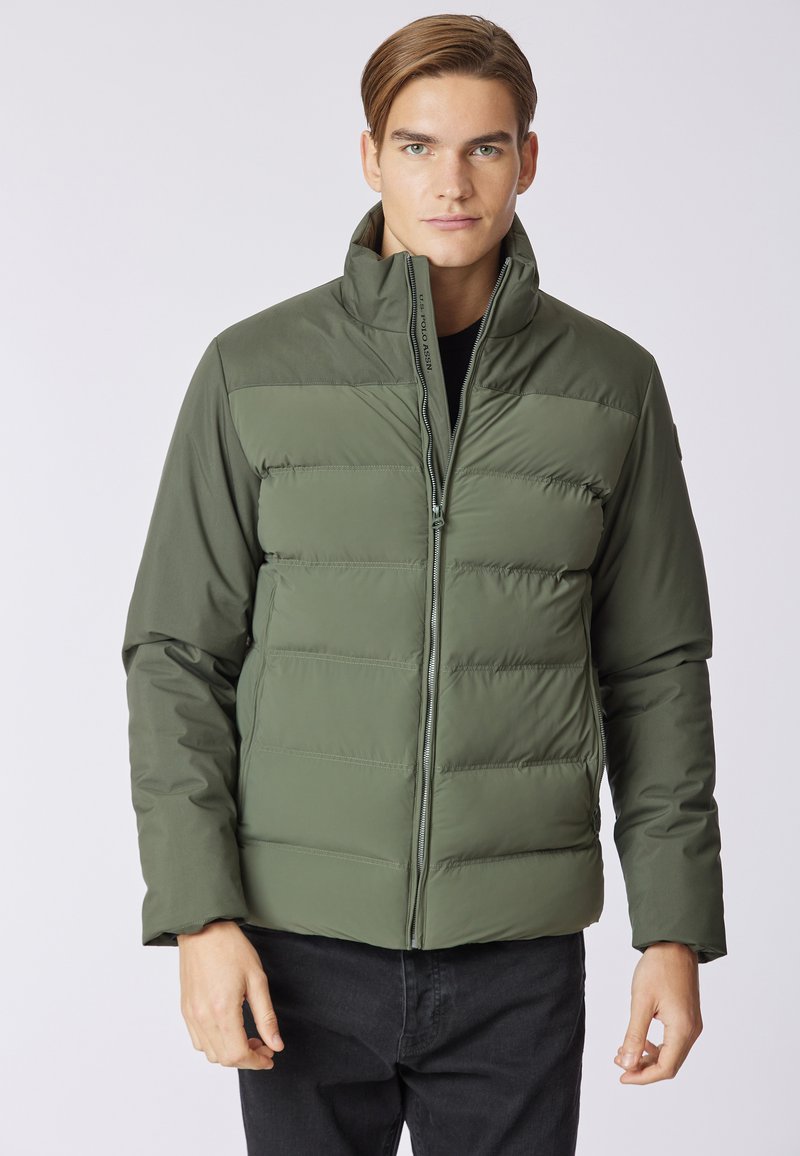 Giacca a vento verde con colletto alto, caratterizzata da sezioni a trapuntatura orizzontale, chiusura con zip e tasche laterali. Tessuto liscio e resistente.