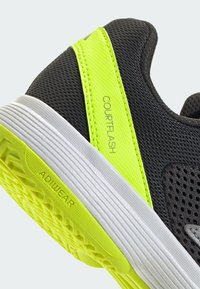 Chaussure de sport noire avec une tige texturée, ornée d'un accent jaune vif et d'une semelle intermédiaire blanche. Comprend les marques "COURTFLASH" et "ADIWEAR".