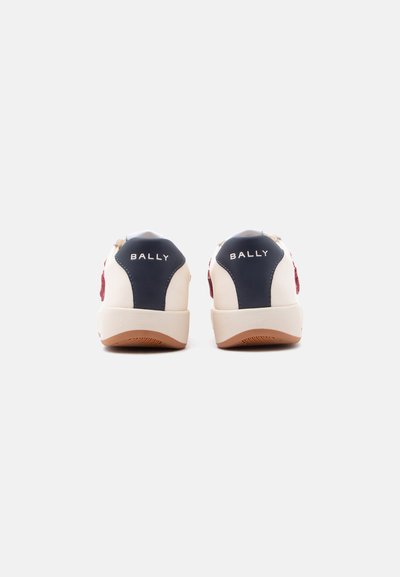 Paire de baskets blanches avec des panneaux de talon bleu marine et le texte « BALLY », vues de dos sur un fond clair uni.