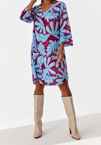 Lyhythihainen mekko V-päällä, jossa on sininen ja viininpunainen lehtikuvio. Yhdistetty polven ylle ulottuviin beigeihin korkokenkiin. Sileä kangas.