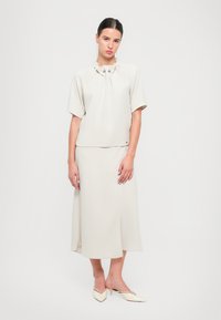 Off-white outfit, ktorý sa skladá z krátkeho rukávu blúzky so zberaným výstrihom a sukne po kolená, v kombinácii s béžovými topánkami s ostrou špičkou.