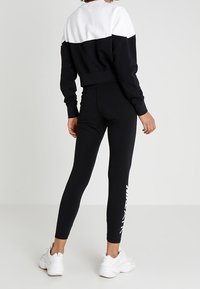 Svart och vit sweatshirt med en kortad design och långa ärmar, kombinerad med svarta leggings som har vit text längs sidan.