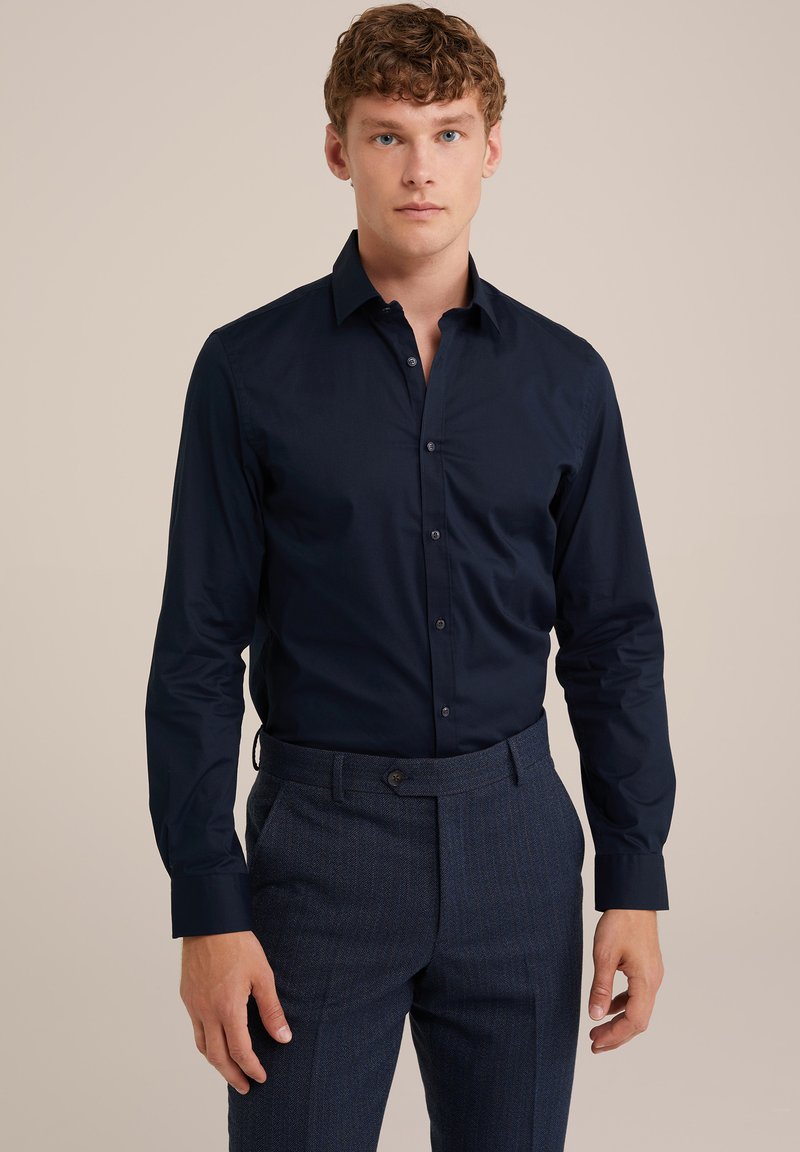 Chemise à manches longues bleu marine avec un col à boutons et des boutons sur le devant, associée à un pantalon foncé texturé. Tissu lisse, design ajusté.
