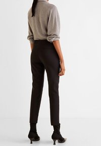 Camicia grigia con maniche arrotolate, abbinata a pantaloni neri a vita alta. Le scarpe presentano punte affusolate e copertura alla caviglia. Design semplice, con accenti minimi.