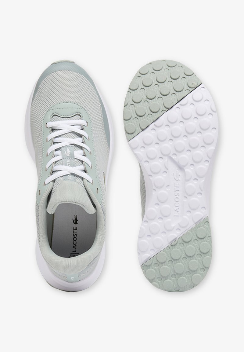 Baskets Lacoste gris clair et blanches avec tige en mesh, lacets blancs et semelle en caoutchouc texturée présentant des motifs circulaires.