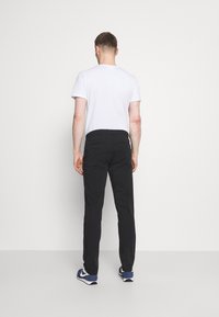 Zwarte broek van duurzaam materiaal, met een recht model, gecombineerd met een eenvoudig wit T-shirt en blauwe sportschoenen. Geen opvallende patronen.