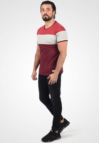 Kortermet t-skjorte med røde, grå og mørkerøde fargeblokker. Har rund halslinning og en myk tekstur. Kombinert med slim-fit svarte jeans og svarte sneakers.