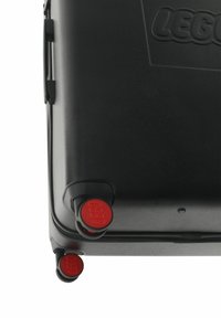 Black hard-shell case with LEGO branding, featuring two black wheels with red accents and a textured surface. Zipper closure visible.