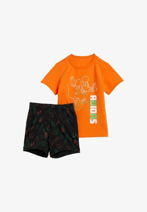 Oranje katoenen t-shirt met een witte Mickey Mouse afbeelding en 'ADIDAS' tekst; gecombineerd met zwarte shorts met kleurrijke patronen van sportuitrusting en Mickey.