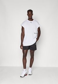 Hvid oversized T-shirt med sort Puma-logo, parret med sorte shorts og hvide træningssko. Glat stof med afslappet pasform.