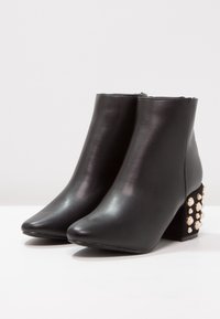 Schwarze Leder-Ankle-Boots mit spitzen Zehen und Blockabsätzen. Der Absatz ist mit Verzierungen aus Kunstperlen für zusätzliche Details ausgestattet.