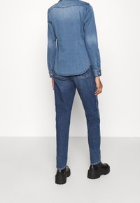 Jeansskjorta och jeans set, ljusblå. Skjortan har en rundad nederkant och knappribbor; jeansen har en rak passform med subtila sidodetaljer. Svarta kraftiga kängor.