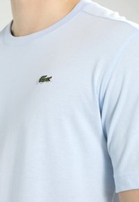 Világoskék pamut póló kerek nyakkal és rövid ujjakkal. Apró zöld hímzett krokodil logó található a mellkasán.