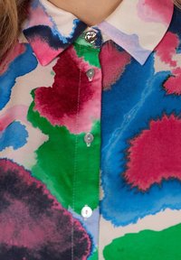 Kraagshirt met een veelkleurig abstract patroon in blauw, groen, roze en zwart, met knopen en een gladde stofstructuur.