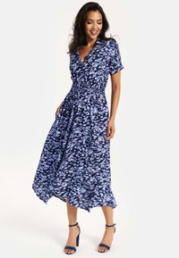 Blue and white patterned maxi dress with short sleeves, a V-neck, and smocked waist design. Finished with a flowy hemline. No accessories visible.
