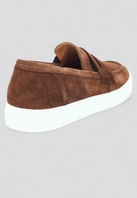 Brązowy zamszowy but wsuwany z białą gumową podeszwą, z zaokrąglonym noskiem i luźnym fasonem cholewki. Lekko teksturowana powierzchnia.
