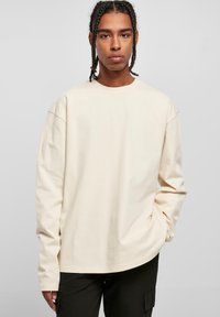 Langermet beige t-skjorte laget av bomull, med en avslappet passform, rund hals og senkede skuldre. Kombinert med mørke cargo-bukser.
