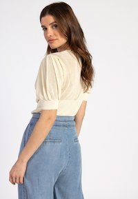 Crème gebreide top met pofmouwen, in combinatie met lichtblauwe high-waisted denim broek met zijzakken en een gladde textuur.