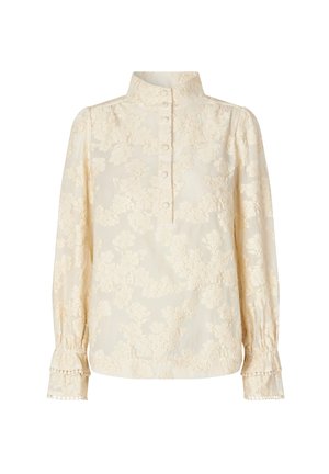 Blusa color crema con patrón de encaje floral, cuello alto, placket de botones y mangas largas con puños fruncidos y borde festoneado.
