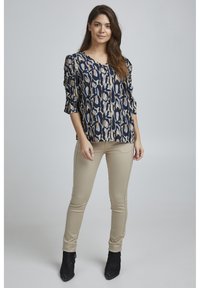 Blusa navy con motivo astratto beige, dal taglio ampio e maniche a sbuffo. Abbinata a pantaloni beige aderenti e stivali neri alla caviglia.