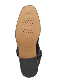 Suela de zapato negra con una superficie de goma suave en tono marrón, que presenta orificios de ventilación para transpirabilidad y el logotipo de la marca grabado en el talón.