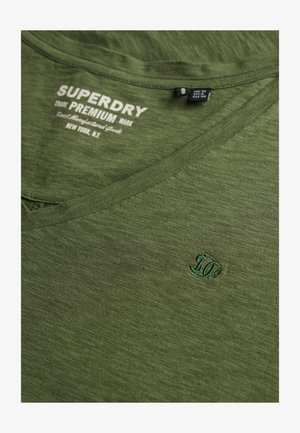 Olijfgroene V-hals T-shirt van zacht materiaal, met een klein borduursel in donkerder groen en een bedrukte label bij de hals.