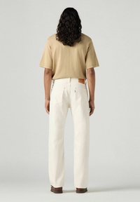 Beige short-sleeve shirt with a relaxed fit, paired with white straight-leg jeans featuring back pockets and a leather logo patch.