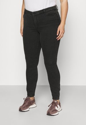 Person wearing black skinny jeans and mauve New Balance sneakers, standing against a plain white background.