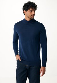 Suéter de cuello alto azul marino hecho de un material suave, con mangas largas y un diseño ajustado, combinado con jeans oscuros.