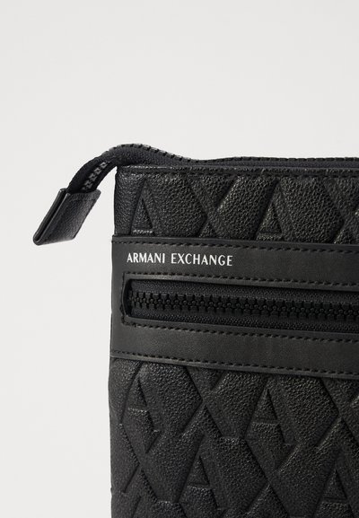 Pochette noire en simili cuir texturé avec un motif géométrique en relief, dotée d'une poche zippée et marquée "Armani Exchange."