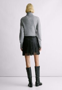 Maglione a collo alto grigio e luccicante con maniche lunghe abbinato a una gonna plissettata in pelle nera e stivali alti fino al ginocchio in pelle nera.