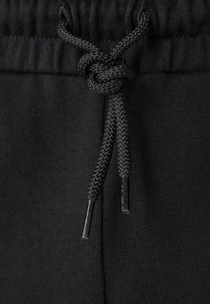 Coulisse nera annodata in un nodo sulla vita di pantaloni o pantaloncini in tessuto a coste nero.