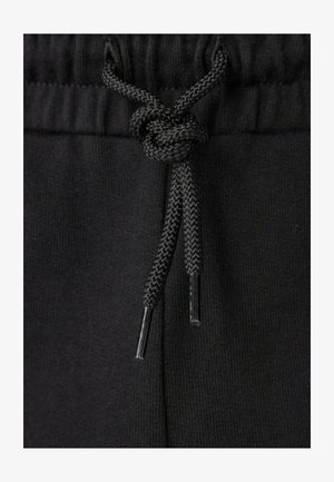 Coulisse nera annodata in un nodo sulla vita di pantaloni o pantaloncini in tessuto a coste nero.