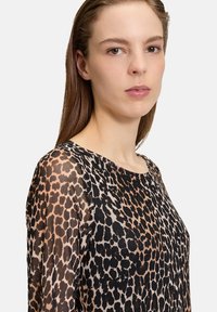 Blouse imprimé léopard avec un design transparent, un col rond et des manches longues, dans des nuances de noir et de marron.