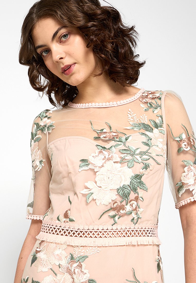 Abito rosa pallido con maniche trasparenti, ricami floreali in verde e pesca, bordo in pizzo in vita e scollatura impreziosita da perle.