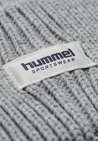Grått stickat tyg med framträdande ribbad struktur. En vit etikett visar "hummel" i mörkblått, med "SPORTSWEAR" under.