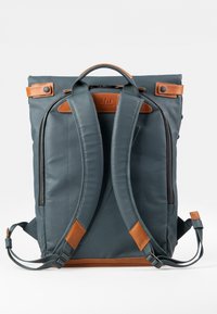 Zaino in tessuto blu scuro con dettagli in pelle marrone. Presenta spallacci imbottiti, scomparti con doppia zip e una maniglia superiore.