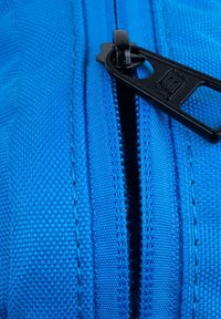 Funda de tela azul con cremallera negra, que presenta un material texturizado y costuras visibles a lo largo de los bordes.