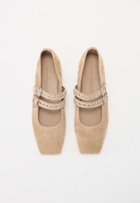 Beige semsket Mary Jane-sko med firkantet tå, to dekorative stropper med sølvfargede hull og spenner. Myk tekstur, minimalistisk design.
